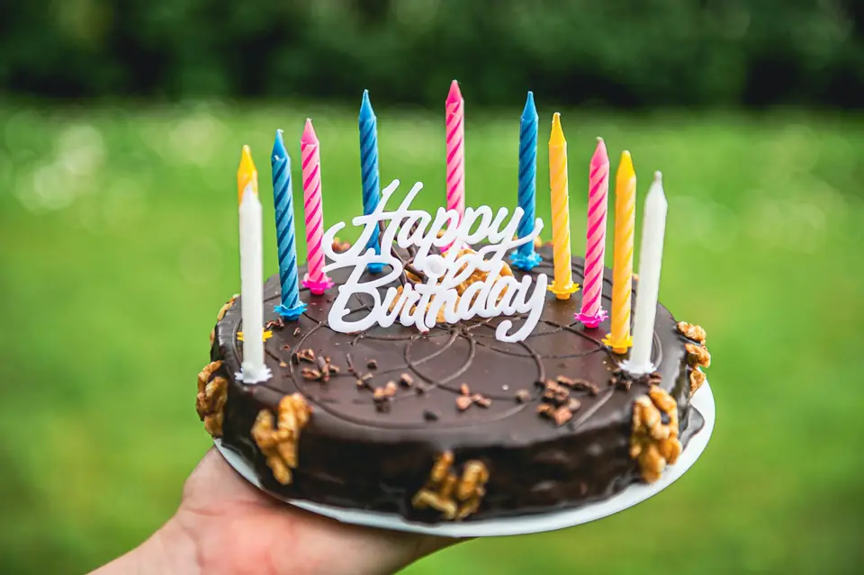 A chocolate birthday cake with candles, held up outdoors